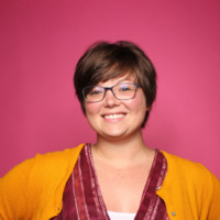 Woman smiling wearing yellow cardigan in front of pink background